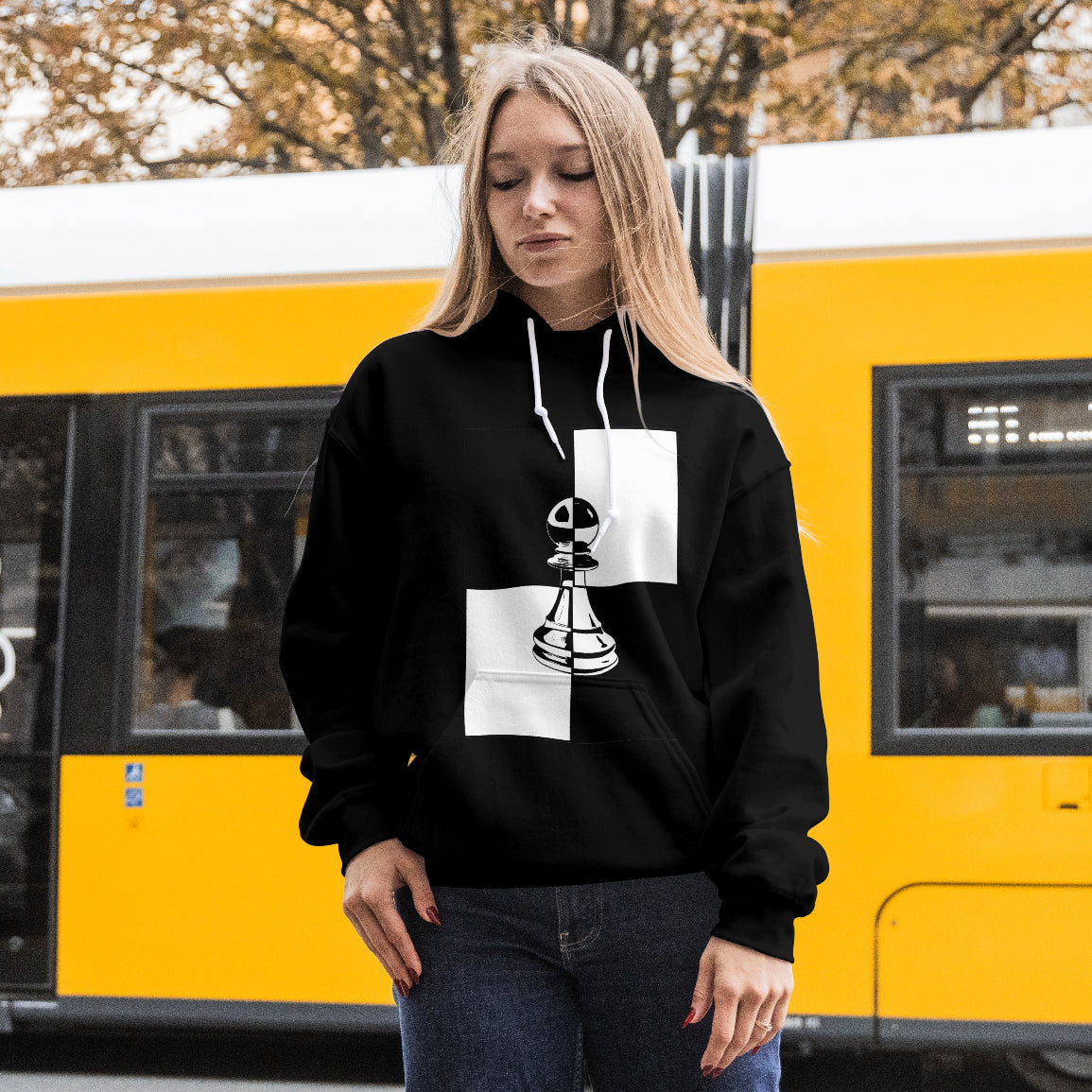 Person wearing a black hoodie with a unique design in front of a yellow train.