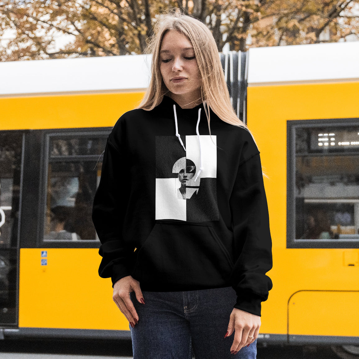 Person wearing a black hoodie with a white graphic design in front of a yellow train.