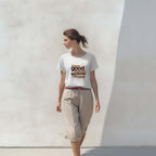 Woman wearing a white t-shirt with text standing against a plain wall.