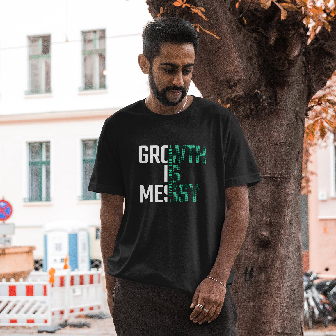 Man wearing a black t-shirt with 'GROWTH IS MESSY' text, standing outdoors.