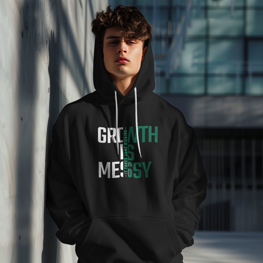 Person wearing a black hoodie with text that reads growth is messy, standing against a modern building.