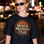 A woman wearing a black graphic t-shirt with a circular 'Mental Mayhem Club' logo, standing on a blurred city street at night.