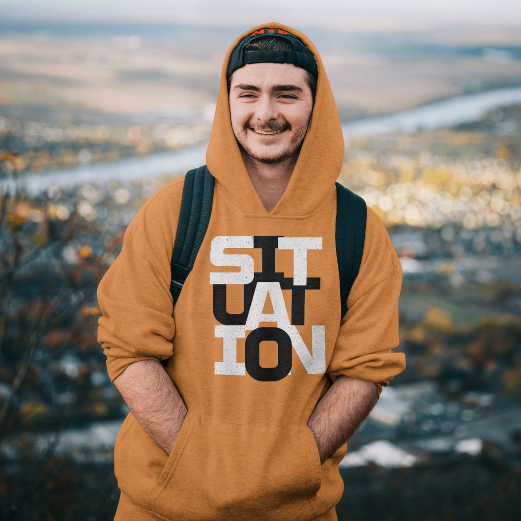 Person wearing a mustard yellow hoodie with text, standing outdoors with a scenic background