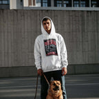 Man wearing a white hoodie with a graphic design, standing outdoors with a dog on a leash.