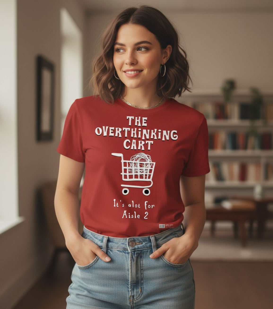 Woman wearing a red t-shirt with a graphic and text, standing in a room with a bookshelf.
