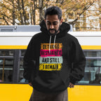 Man wearing a black hoodie with text in front of a yellow and gray bus.