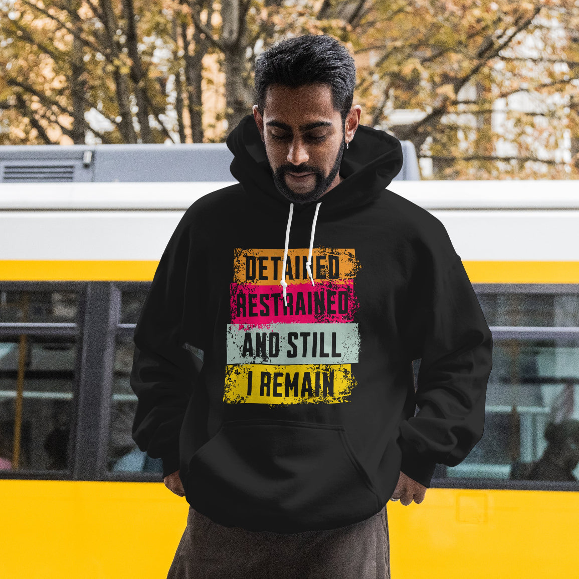 Man wearing a black hoodie with text in front of a yellow and gray bus.