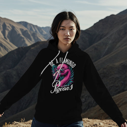 Person wearing a black hoodie with a flamingo design and text, standing against a mountainous landscape.