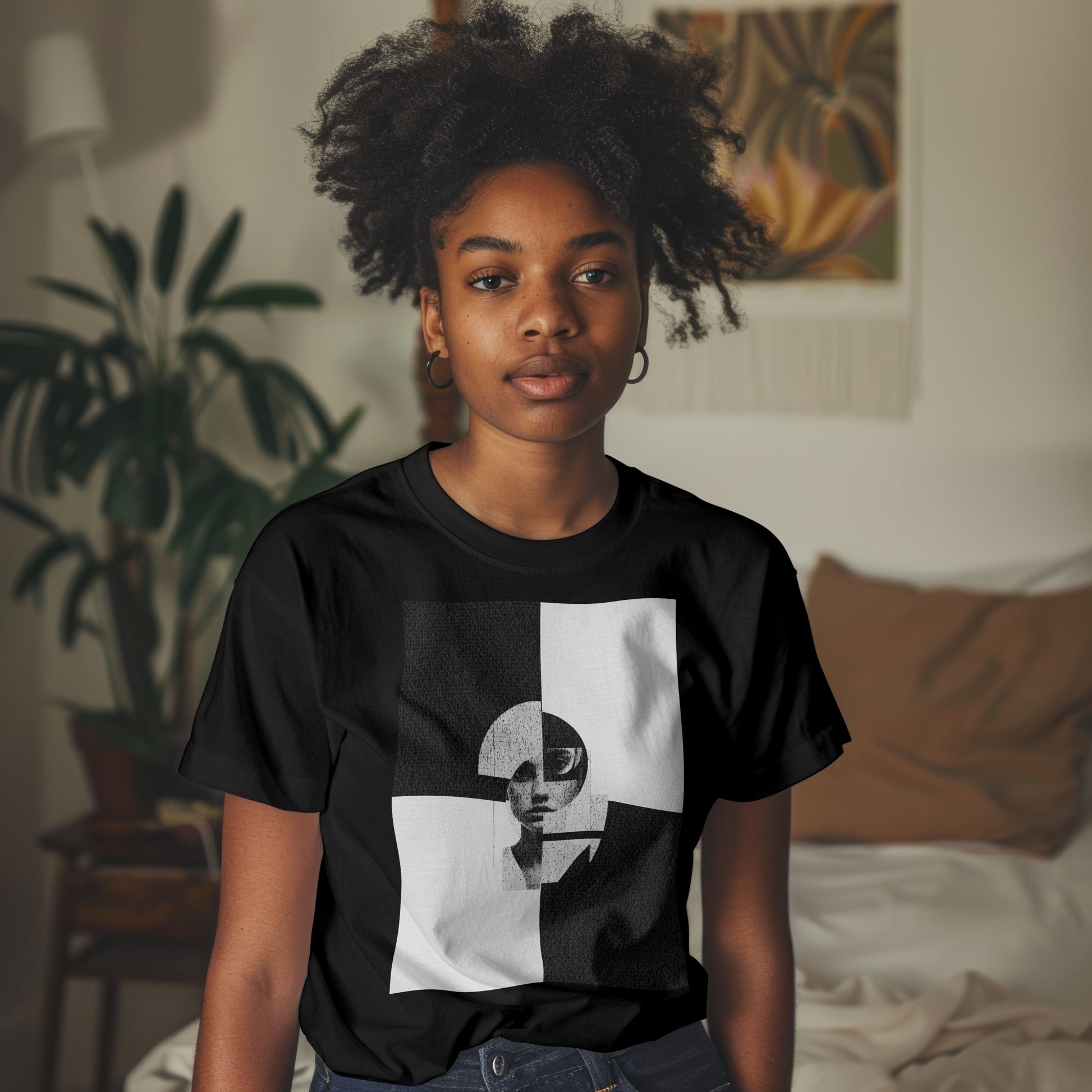 Person wearing a black t-shirt with a graphic design in a room with plants and a bed.