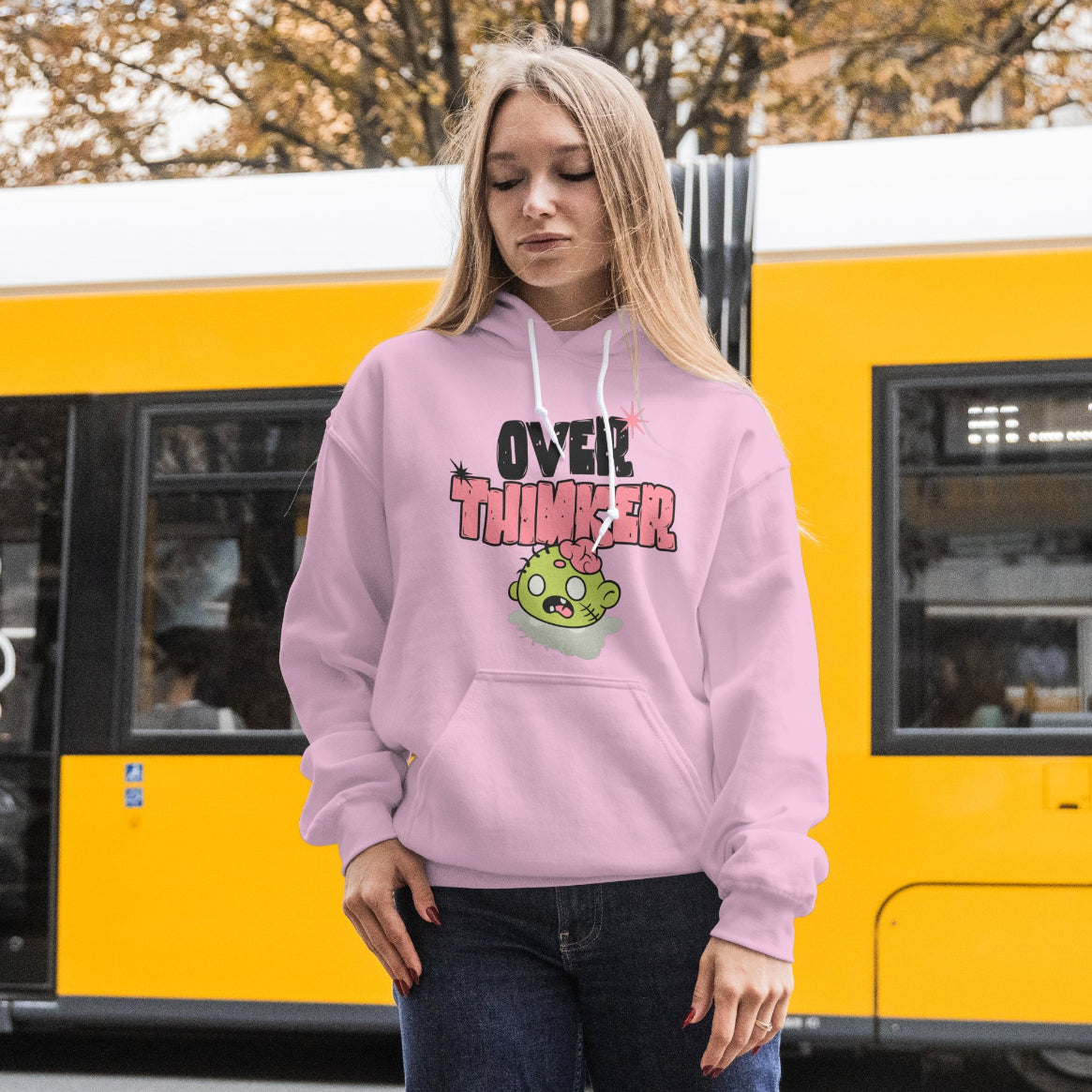 A person wearing a pink hoodie with text and a cartoon character, standing in front of a yellow tram.