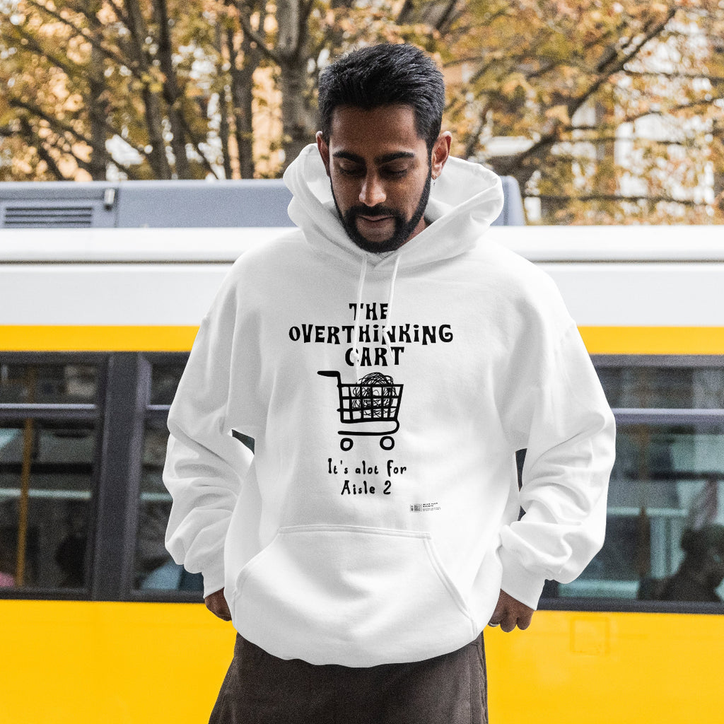 Man wearing a white hoodie with text that reads "the overthinking cart" and graphics, standing in front of a yellow and gray bus.