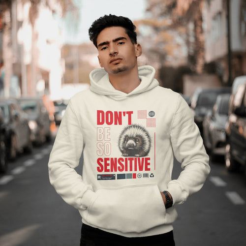 Man wearing a hoodie with a hedgehog graphic and text that reads "don't be so sensitive" on a city street.