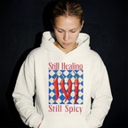 Person wearing a white hoodie with chili pepper design and text 'Still Healing, Still Spicy' on a black background